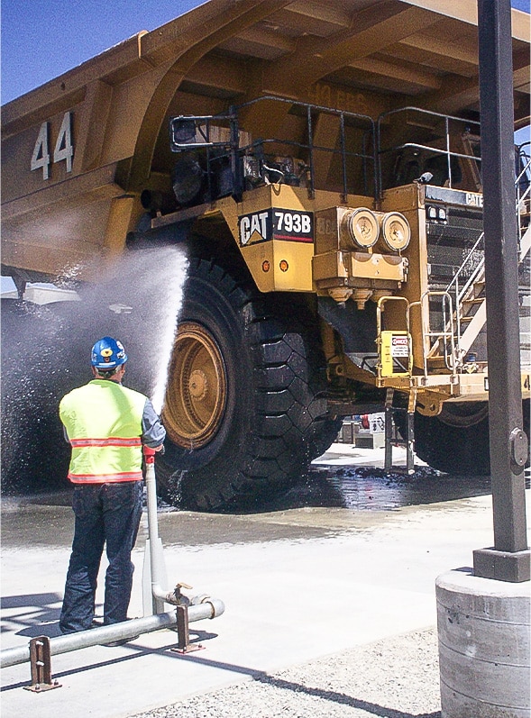 Large mining truck being washed manually by on-site worker