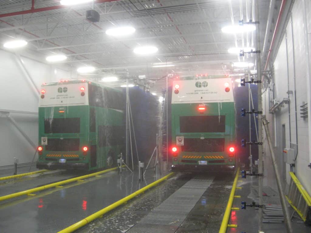 Two buses driving through wash systems.
