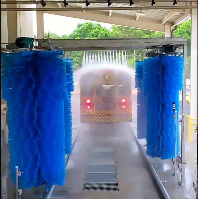 A yellow school bus being washed by a transit bus washing machine.