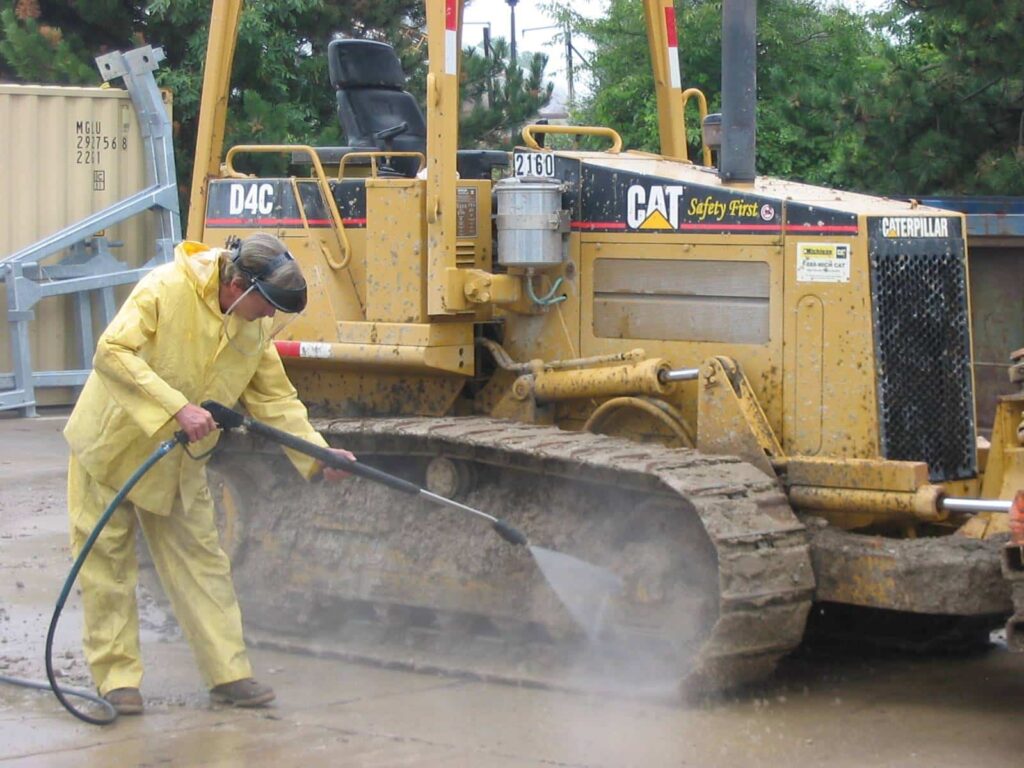 A man washing a mine vehicle with a high-pressure spray.