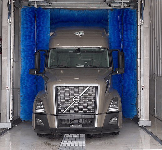 The front of a grey truck going through a commercial truck wash system.
