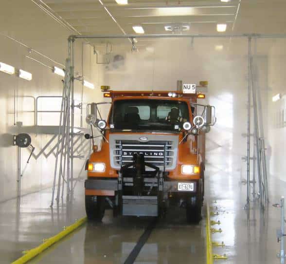 An orange truck going through an automatic truck wash system.