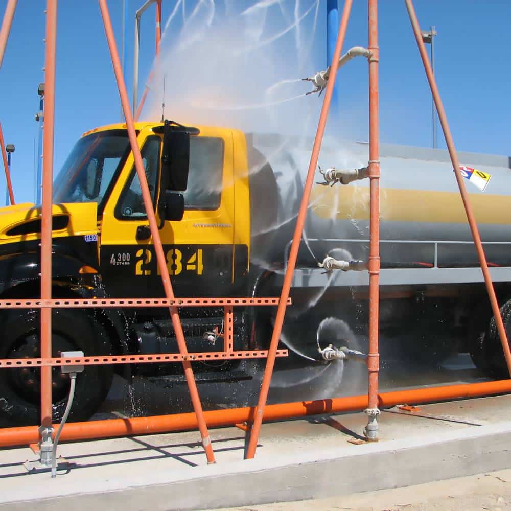 A yellow truck being washed by an automatic truck wash system.